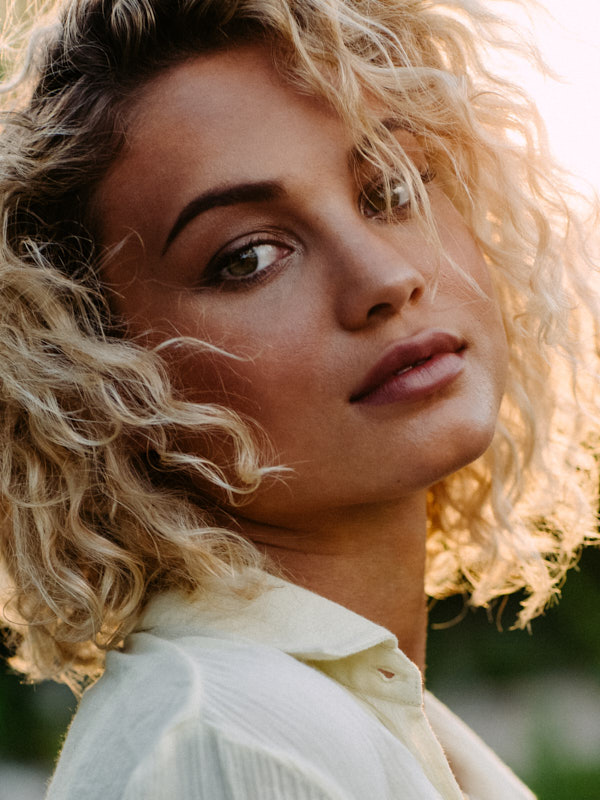 Backlit close portrait of a woman with curly blonde hair