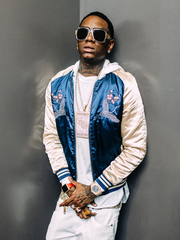 Man in a blue satin bomber jacket and sunglasses against a grey wall