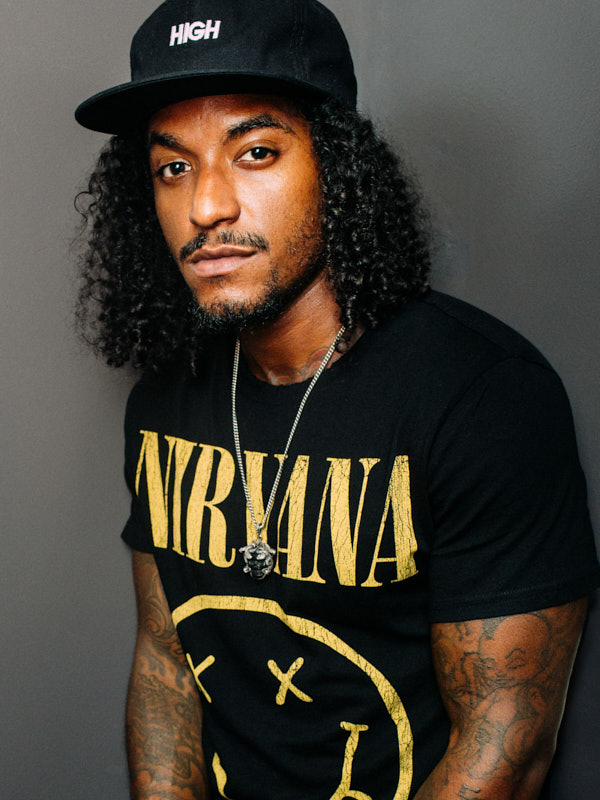 Portrait of a man in a black cap and graphic tee against a grey wall
