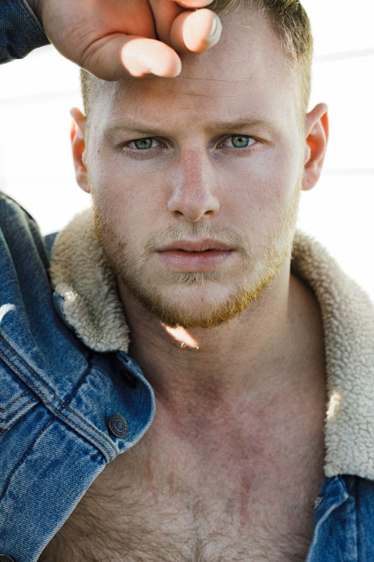 Close portrait of a man in a shearling-collared denim jacket, hand raised to his brow